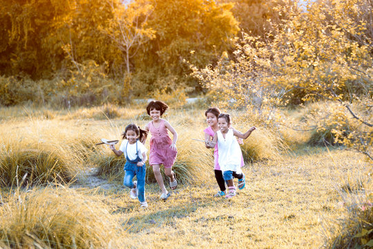 Happy asian children having fun to run and play with toy paper airplane in the meadow  together in summer time