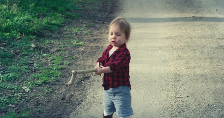 Little toddler boy with stick on path in nature