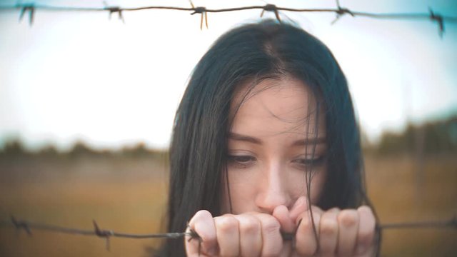girl brunette refugee behind barbed wire lifestyle camp slow motion video. the concept of freedom is upset Woman hands and barbed wire. girl Refugee, prison, refugees captivity concept
