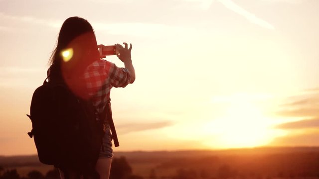 Hipster hiker lifestyle silhouette girl is shooting video of beautiful nature sundown on cell telephone smartphone slow motion video. Female tourist is taking photo with mobile phone camera. female