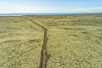 Aerial view of Iceland road crossing through green moss nature landscape background towards ocean cliff. Travel adventure vacation concept. Off road cross country driving.