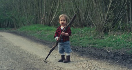 Little boy standing on path in forest with a big stick