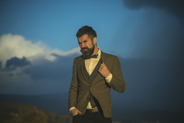 Hipster in classic coat with bow tie hiking in mountains on summer vacation. Hipster with beard and...