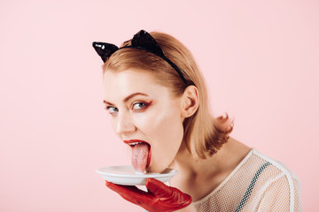 kitten girl in ears and red gloves with yoghurt on pink background. kitten woman lick milk.