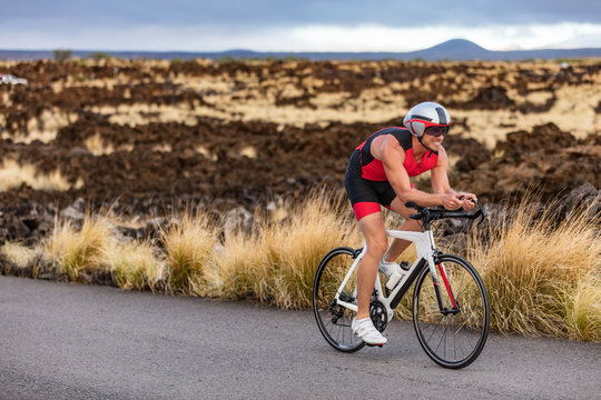 Triathlon professional cyclist man cycling road racing bike in time trial helmet and compression tri suit in Hawaii landscape for Kailua-Kona ironman. Triathlete biking in nature.