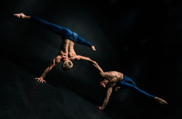 Male acrobatic duo performs a complicated balancing act on a dark background