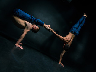 Male acrobatic duo performs a complicated balancing act on a dark background