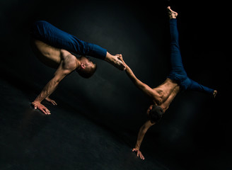 Male acrobatic duo performs a complicated balancing act on a dark background