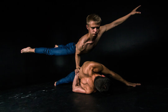 Male acrobatic duo performs a complicated balancing act on a dark background