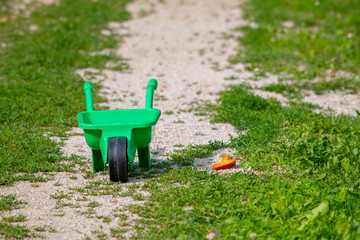 Toy wheelbarrow with shovel on grass, abandoned toy