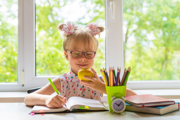 Little girl with school supplies is sitting at the table.