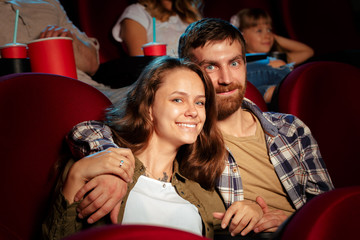 friends sitting in cinema watch film eating popcorn and drinking water.
