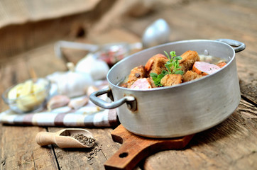 Old saucepan with garlic soup, fresh garlic bulbs, cloves, colored pepper, wooden spoon, croutons, lable and a towel on a rustic wooden table