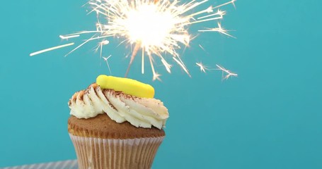 Yellow Birthday cupcake with sprinkles and a sparkler over a blue background. - Powered by Adobe