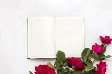 Open diary and red roses on a light stone background. Flat lay, top view