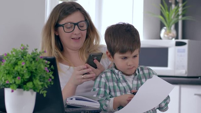 single mother is working at home on computer talking on telephone and taking care of son at same time