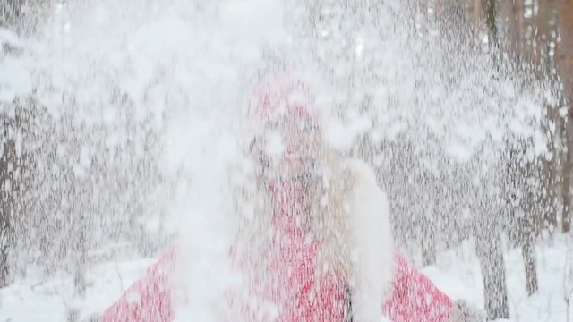 Young woman throws snow up with a nice smile in the winter forest