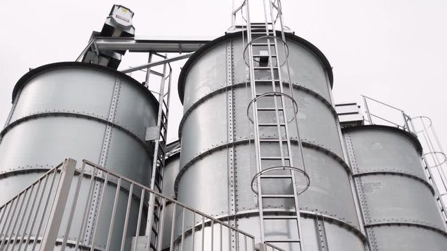 Large gray metal repository construction behind fence at farm facility on cloudy summer day