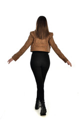 full length portrait of brunette girl wearing brown leather jacket.   standing pose with back to the camera on white background.