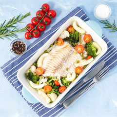Fish cod baked in blue oven with vegetables - broccoli, tomatoes. Healthy diet food. Blue stone background, top view.