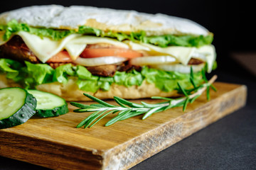 big sandwich on black background rosemary cucumber wooden board Street food, fast food. Homemade burgers with beef, cheese  on the wooden table. Toned image.