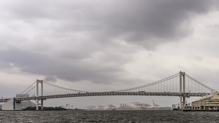 Panoramic view of the Rainbow Bridge in Tokyo, Japan, on a rainy day with cloudy sky