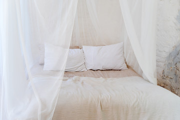 Fototapeta na wymiar Four-poster bed with two pillows. Scandinavian simplicity design. Eco loft apartments.