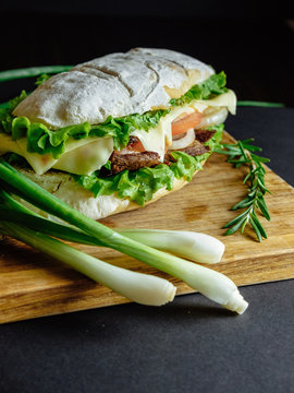 big sandwich on black background rosemary cucumber wooden board green onion Street food, fast food. Homemade burgers with beef, cheese  on the wooden table. Toned image.