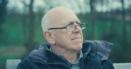 A senior man is sitting on a bench and carefully pondering the vicissitudes of life. 