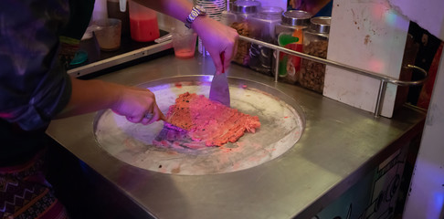 Hand making fruit ice cream on silver metal flat stove. Pan fried ice cream roll vending.