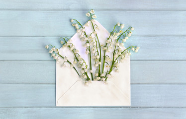 Beautiful flowers white lily of the valley ( Convallaria majalis, lily-of-the-valley, May bells, Mary's tears ) in paper postal envelope on background of blue painted wooden planks. Top view, flat lay
