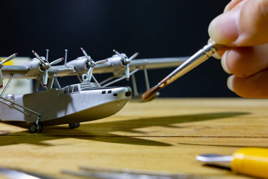 painting plastic model WW2 plane on wooden workbench closeup.