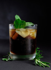 Glass of cola with ice, mint and lemon, rosemary on black background