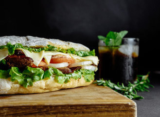 big sandwich  on black background rosemary cucumber wooden board Street food, fast food. Homemade burgers with beef, cheese  on the wooden table. Glass of cola with ice, mint