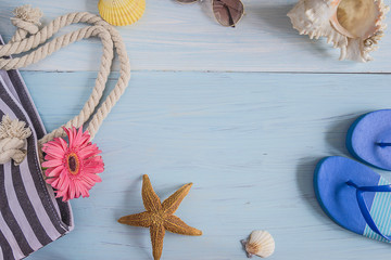 Fototapeta na wymiar Beach holiday concept: bag,seashells,pink flower, sunglasses, blue flip flops, starfish on blue wooden background with copy space