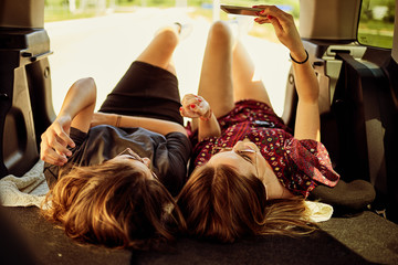 Two girls lying down in the trunk and taking selfie.