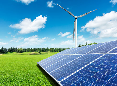 Solar panels and wind turbines in green grass field