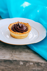 Ruddy tartlet made of shortcake with chocolate ganache on a white porcelain plate