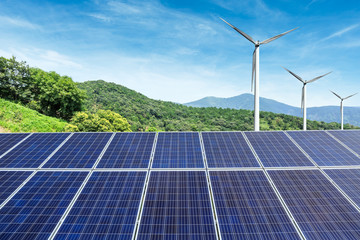 Solar panels and wind turbines with mountains landscape under the blue sky