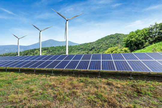 Solar panels and wind turbines with mountains landscape under the blue sky