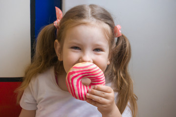 A girl looks at a beautiful glazed donut before eating. She likes to hide part of her face behind a donut. A child plays with food