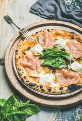 Italian lunch or dinner. Freshly baked pizza with artichokes, smoked turkey ham, olives, cream cheese and basil leaves over rustic wooden background, selective focus, vertical composition
