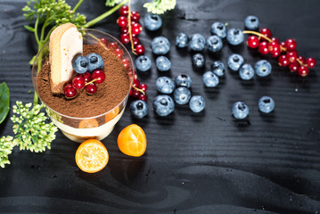 Sweet dessert tiramisu with blueberries and currants on black