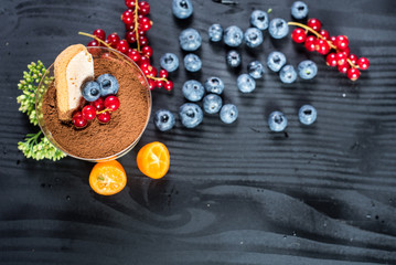 Sweet dessert tiramisu with blueberries and currants on black