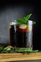 Glass of cola with ice, mint and  rosemary on black background