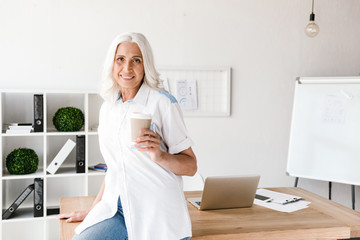 Mature woman indoors in office working drinking coffee