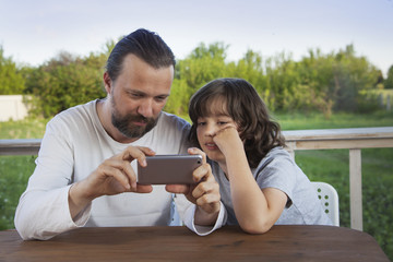 father and son watching the smartphone garden on the terrace on a summer day, family