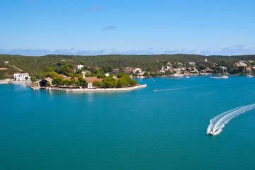 Obraz premium Sea coast of Mahon, Spain. Boats in sea harbor. Naval storehouse and careening wharf. Summer vacation on mediterranean island. Travelling and wanderlust