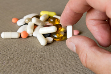 A pill in human hands on the background of a pile of pills. The concept of a healthy lifestyle.
