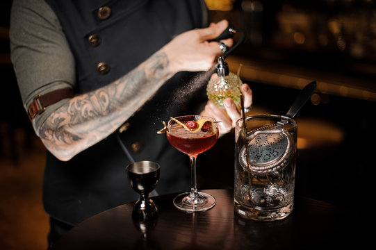 Tattooed bartender spraying on the delicious cocktail with a special liquid